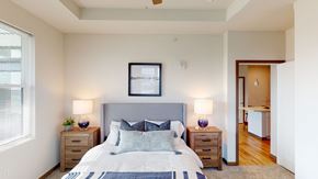 Sun Prairie apartment for rent - A comfortable bedroom here at Van Buren East with soft carpeting and neutral tones. A large window brings in natural light, while a cozy bed and bedside lighting create a warm, inviting atmosphere.