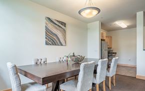 Sun Prairie apartment for rent - A dining area here at Van Buren Place featuring a large wood table, soft gray upholstered chairs, and a warm overhead light that makes the space feel open, inviting, and perfect for gatherings.