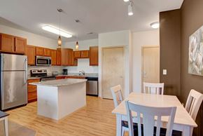Sun Prairie apartment for rent - A dining area here at Van Buren Place featuring a light wood table and matching chairs beside a bright, open kitchen with warm cabinets and an inviting, comfortable layout.