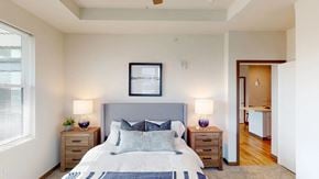 Sun Prairie apartment for rent - A bedroom here at Van Buren West featuring a soft gray upholstered bed, matching wood nightstands, purple glass lamps, and light neutral bedding for a bright, calm, and inviting space.