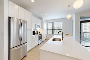 Milwaukee apartment for rent - A bright modern kitchen here at Vim and Vigor with white cabinets, a large island with sink, stainless steel appliances, pendant lighting, and tall windows with blinds bringing in natural light.