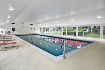 An indoor pool with lounge chairs and tables around the edges, and large windows to the outside courtyard