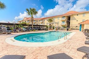 Corpus Christi apartment for rent - A large outdoor swimming pool surrounded by lounge chairs and umbrellas.