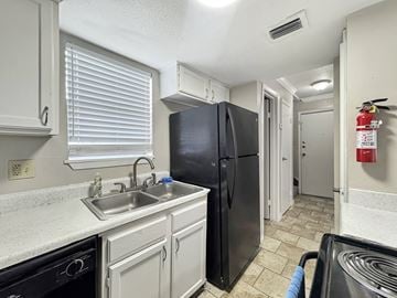 San Antonio apartment for rent - A black refrigerator sits in a kitchen with white cabinets and a black dishwasher.