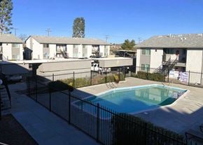 Victorville apartment for rent - A pool surrounded by a black fence in front of apartment buildings.