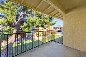Barstow apartment for rent - A balcony with a black railing and a view of a backyard with a tree and a pool.