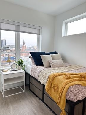 Columbus apartment for rent - A bedroom with a bed, nightstand, and a window overlooking a cityscape.