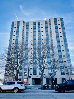 Pekin apartment for rent - A tall building with a white car and a black truck parked in front of it.