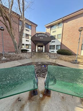 Omaha apartment for rent - A green mesh fence is in front of a building with a sign that says "Camelot EZ".