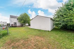 Mayfield Heights house for rent - A white house with a metal garage is surrounded by greenery.