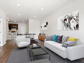 Hardwood floored living room with can lights and view of kitchen.