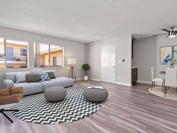 Reseda apartment for rent - A living room with a grey sofa, a black and white rug, a grey ottoman, a dining table with chairs, and a ceiling fan.