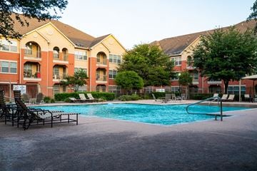 San Antonio apartment for rent - A large swimming pool is surrounded by lounge chairs and trees in front of apartment buildings.