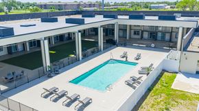 Mitchell apartment for rent - A large outdoor swimming pool surrounded by sun loungers and a white building.
