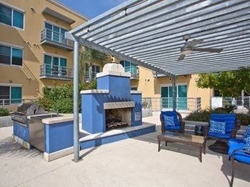 A patio with a fireplace and blue chairs and a pergola
