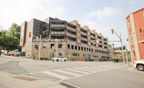 Cambridge apartment for rent - A modern building with a mix of brick and panel construction is situated on a street corner with a crosswalk in front.