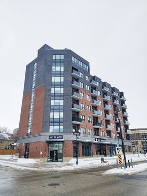 Kitchener apartment for rent - A tall building with a red brick base and a black top with the words KC PLACE on it.