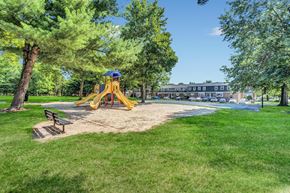 Hillsborough apartment for rent - Exterior photo of Beekman Garden in Hillsborough, NJ showing the community playground, surrounded by grass and trees with a bench for relaxing.