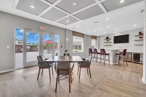 Belle Mead apartment for rent - Interior photo of one of the community spaces at Meadows at Montgomery showing a luxury vinyl tile floor and multiple seating areas. Ther is a large screen TV on the wall, and doors leading out to the community patio with seating and grills.