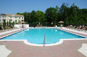 West Windsor apartment for rent - Princeton Terrace swimming pool photo showing a very large pool with reclining chairs located on both sides surrounded by a fence. The apartment building can be seen in the background. Several trees highlight the landscaping.