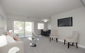 Newark apartment for rent - A living room with a grey couch, a coffee table, a dining table with chairs, and a flat screen TV mounted on the wall.