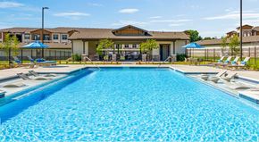 Grand Prairie apartment for rent - A large swimming pool in front of a building with a fence and umbrellas.