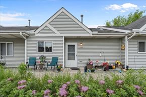 Forest Lake apartment for rent - A house with a grey exterior and a white door is surrounded by a garden with pink flowers.