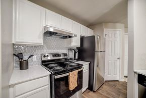 San Antonio apartment for rent - White-cabinet kitchen with patterned tile backsplash, electric range, and stainless refrigerator.