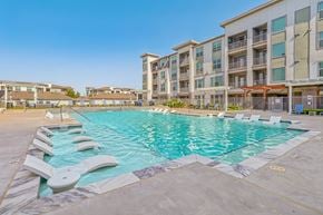 Wylie apartment for rent - A large swimming pool with lounge chairs is surrounded by apartment buildings.