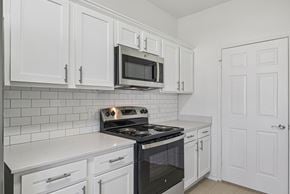 Waxahachie townhouse for rent - A kitchen with white cabinets and a black stove top oven.