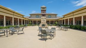 Lewisville apartment for rent - A courtyard with tables and chairs and a building in the background.