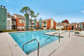 Oklahoma City apartment for rent - A swimming pool surrounded by a concrete floor and metal railings with apartment buildings in the background.