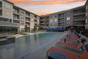 Mckinney apartment for rent - A swimming pool surrounded by sun loungers and umbrellas in front of apartment buildings.