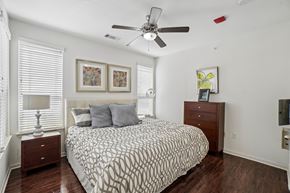 Dallas apartment for rent - A bedroom with a patterned bedspread, a ceiling fan, and a nightstand with a lamp.