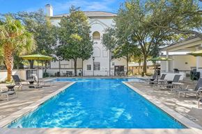 Dallas apartment for rent - A large swimming pool surrounded by lounge chairs and trees.