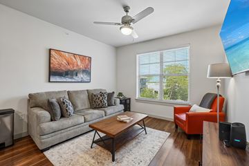 Garland apartment for rent - A living room with a grey couch, a red chair, a coffee table, and a painting on the wall.