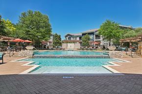 Dallas apartment for rent - A large outdoor swimming pool surrounded by a stone wall and seating areas.