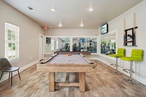 Fort Worth apartment for rent - A pool table is in the middle of a room with a chair and a TV mounted on the wall.