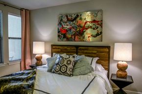 San Antonio apartment for rent - A bedroom with a large bed, two lamps, and a colorful painting on the wall.