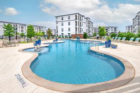 Aubrey apartment for rent - A large outdoor swimming pool surrounded by lounge chairs and buildings in the background.