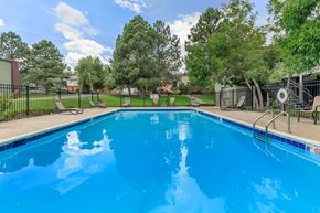 Lakewood apartment for rent - A blue swimming pool surrounded by a black fence and trees.