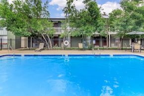 Lakewood apartment for rent - A swimming pool surrounded by trees and a building in the background.