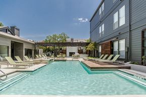 Dallas apartment for rent - a pool with lounge chairs and a hot tub in front of a building