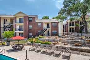 Austin apartment for rent - A pool area with chairs and a red umbrella in front of apartment buildings.