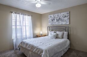 Austin apartment for rent - A bedroom with a bed, pillows, a ceiling fan, and a painting on the wall.