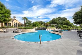 Austin apartment for rent - Resort-style pool with curved edge, stone landscaping, and wide sun deck seating.