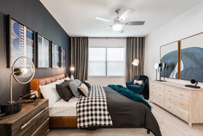 Austin apartment for rent - Primary bedroom with ceiling fan, upholstered bed, accent wall, and large window.
