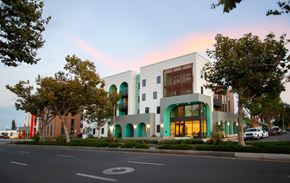 Santa Ana townhouse for rent - A modern building with a white facade and green accents is surrounded by trees and parked cars.