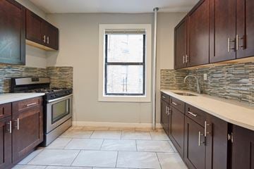 Bronx apartment for rent - A kitchen with dark wood cabinets and a stone backsplash.