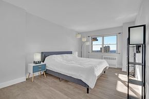 Asbury Park apartment for rent - A bedroom with a bed, nightstand, and a window overlooking the city.
